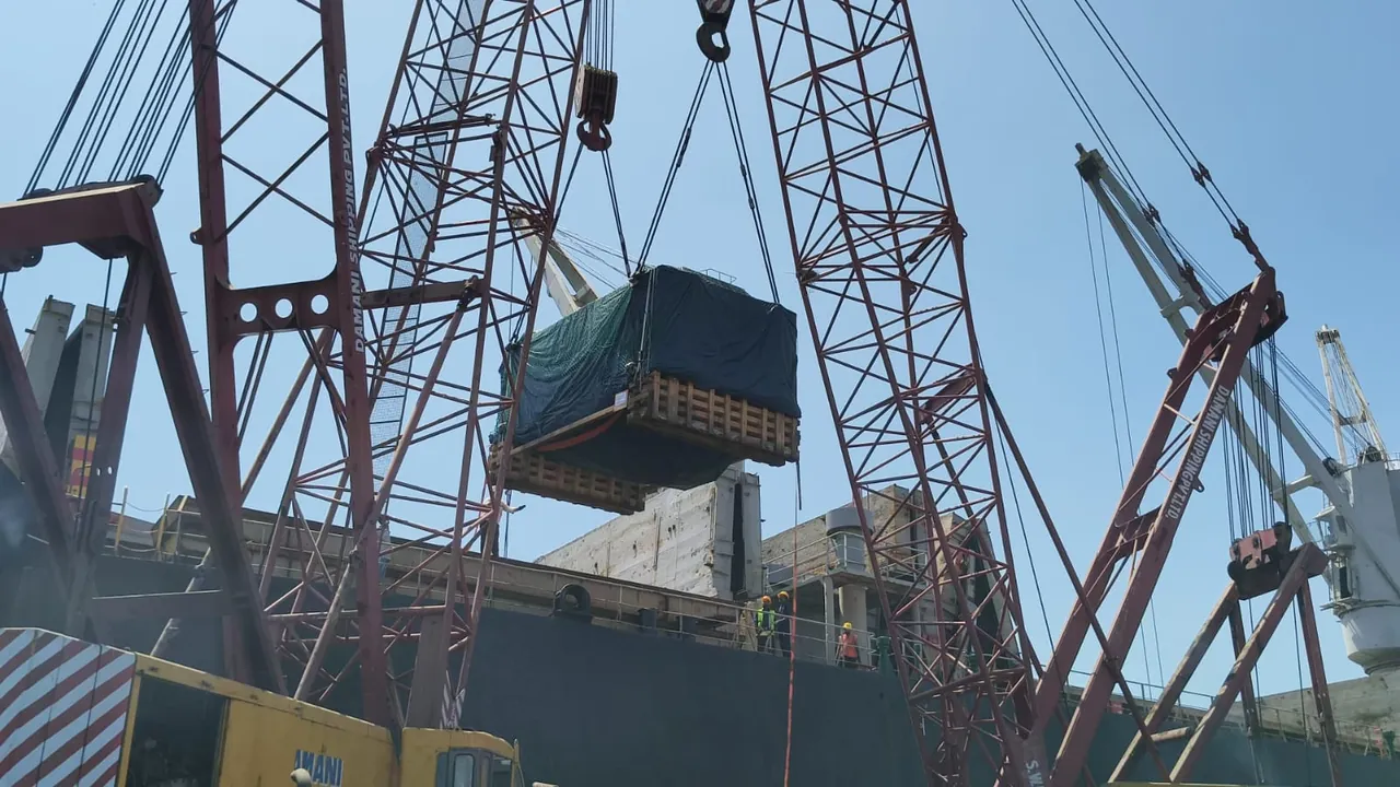 Covered project cargo on a wooden base being lifted by cranes onto a vessel