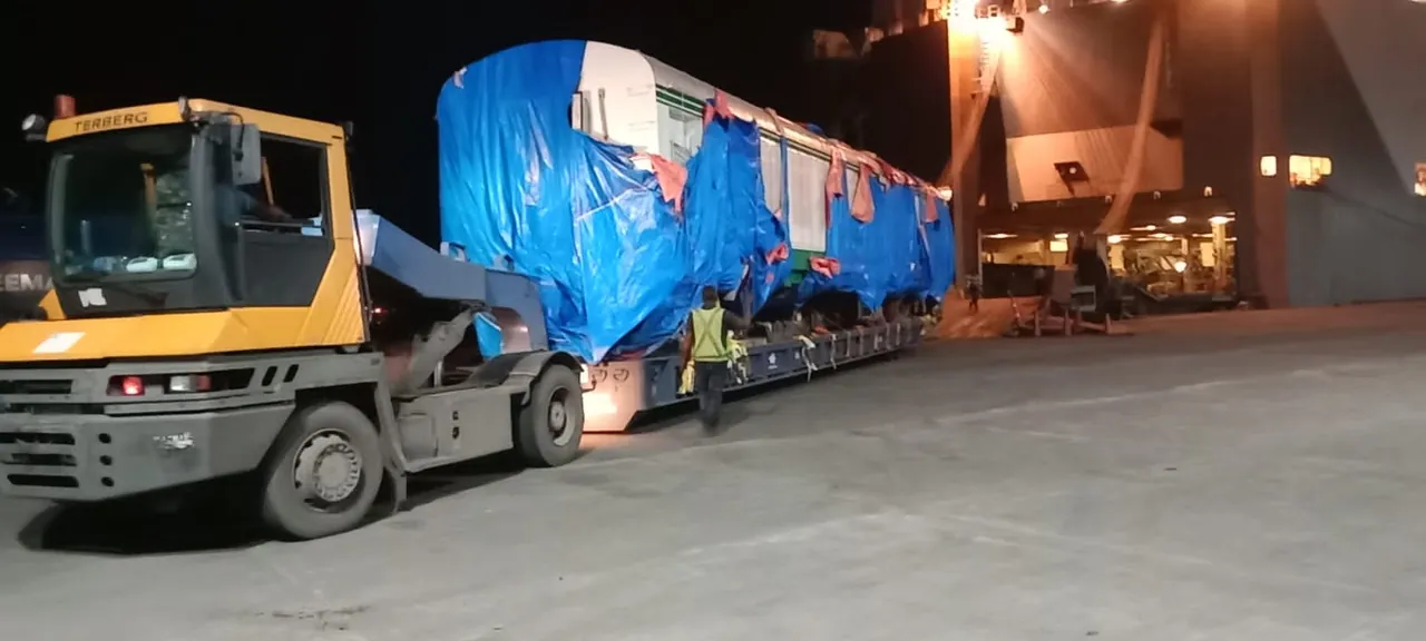 Railway coach wrapped in tarpaulin on a trailer at the port at night