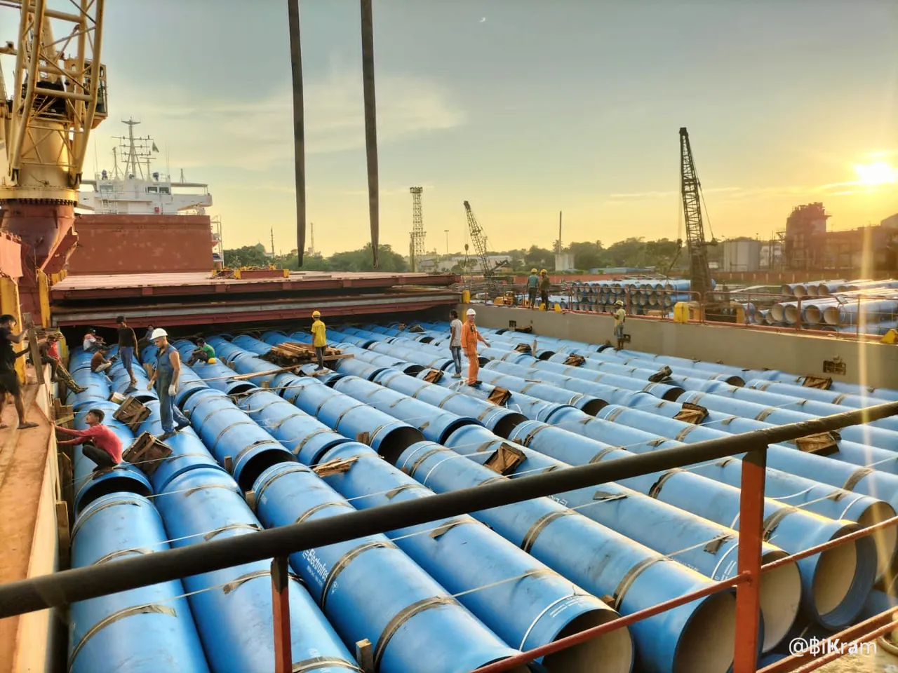 Blue pipes stowed in the hold of a vessel with workers on deck