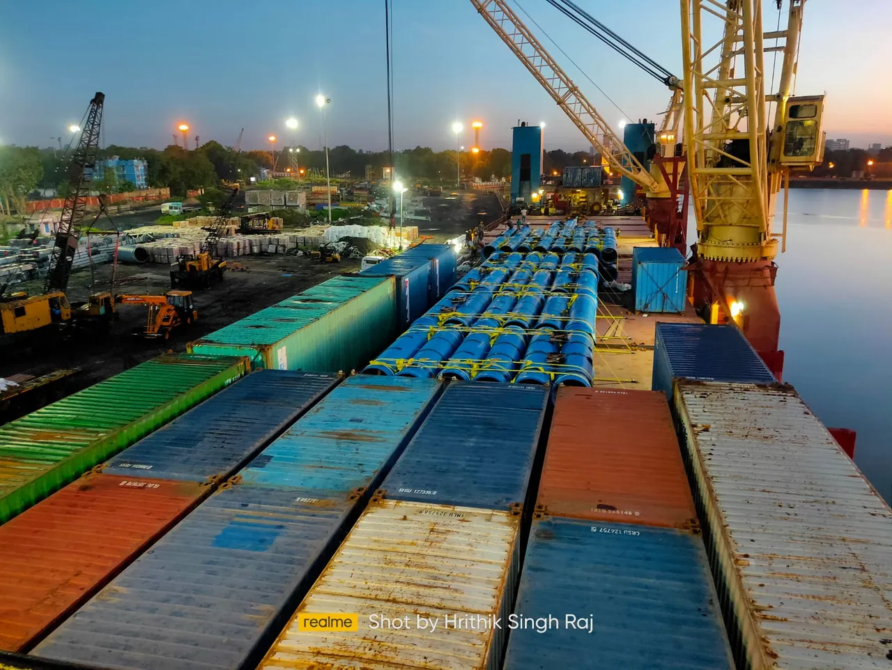 Vessel deck loaded with containers and pipes at dusk